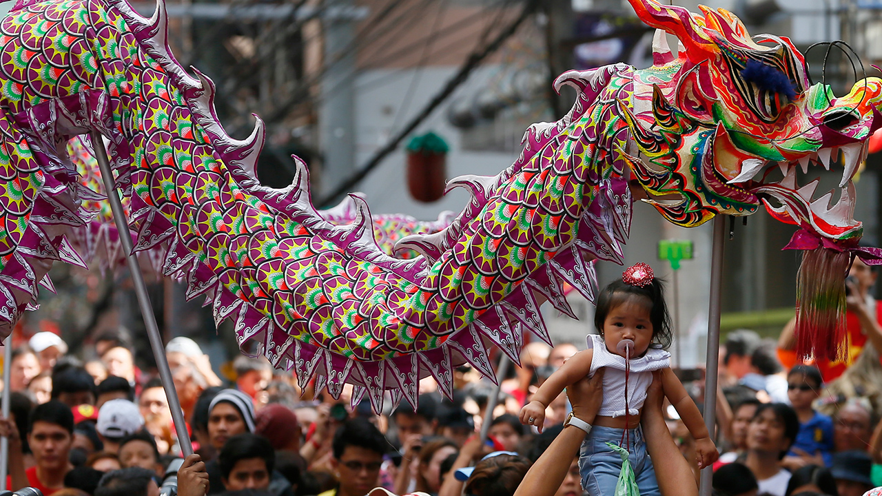 A reveler raises a baby as dragon dancers make their through a crowd to perform in celebration of the Chinese Lunar New Year Monday, Feb. 8, 2016 at Manila's Chinatown district