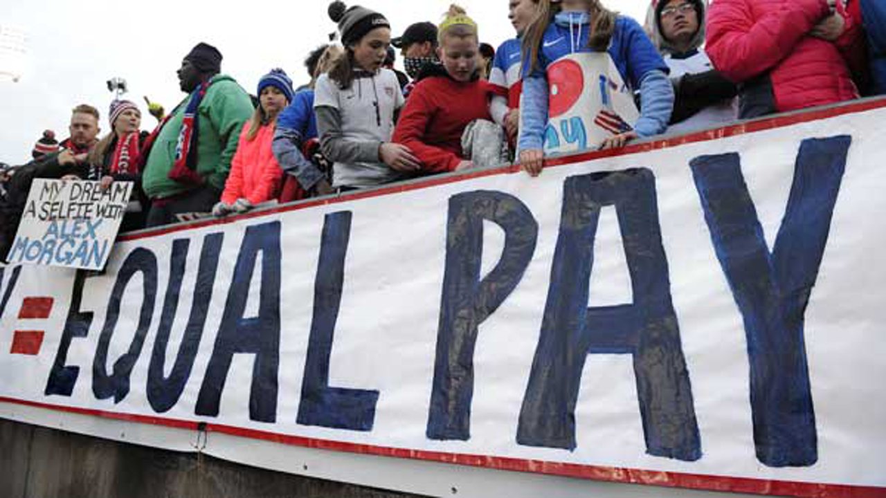 Fans stand behind a large sign for equal pay for the women's soccer team during an international friendly soccer match between the United States and Colombia.