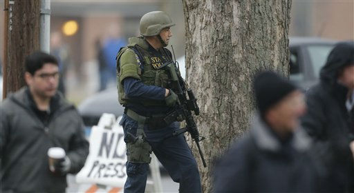 A Conn. State Police tactical team officer takes cover behind a tree as the area around St. Rose of Lima Catholic Church is searched in Newtown, Conn., Sunday, Dec. 16, 2012 after a there was a bomb threat. A gunman opened fire at Sandy Hook Elementary School in the town, killing 26 people, including 20 children before killing himself on Friday. (AP Photo/Charles Krupa)