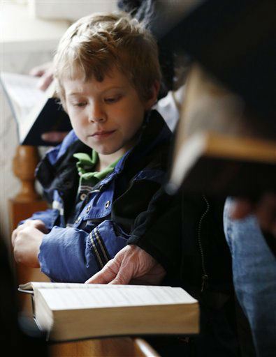 A child looks on as people read from prayer books during a service in honor of the victims who died a day earlier when a gunman opened fire at Sandy Hook Elementary School in Newtown, Conn., as people gathered at St. John's Episcopal Church , Saturday, Dec. 15, 2012, in the Sandy Hook village of Newtown, Conn. The massacre of 26 children and adults at Sandy Hook Elementary school elicited horror and soul-searching around the world even as it raised more basic questions about why the gunman, 20-year-old Adam Lanza, would have been driven to such a crime and how he chose his victims. (AP Photo/Julio Cortez)