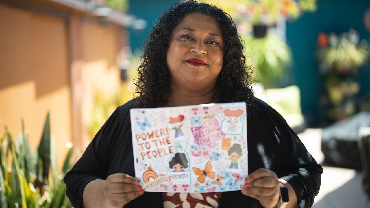 Artist Claudia Ramos holds up a journal featuring the protest collection of her Latinx stationery brand Hola Mijas Bonitas.