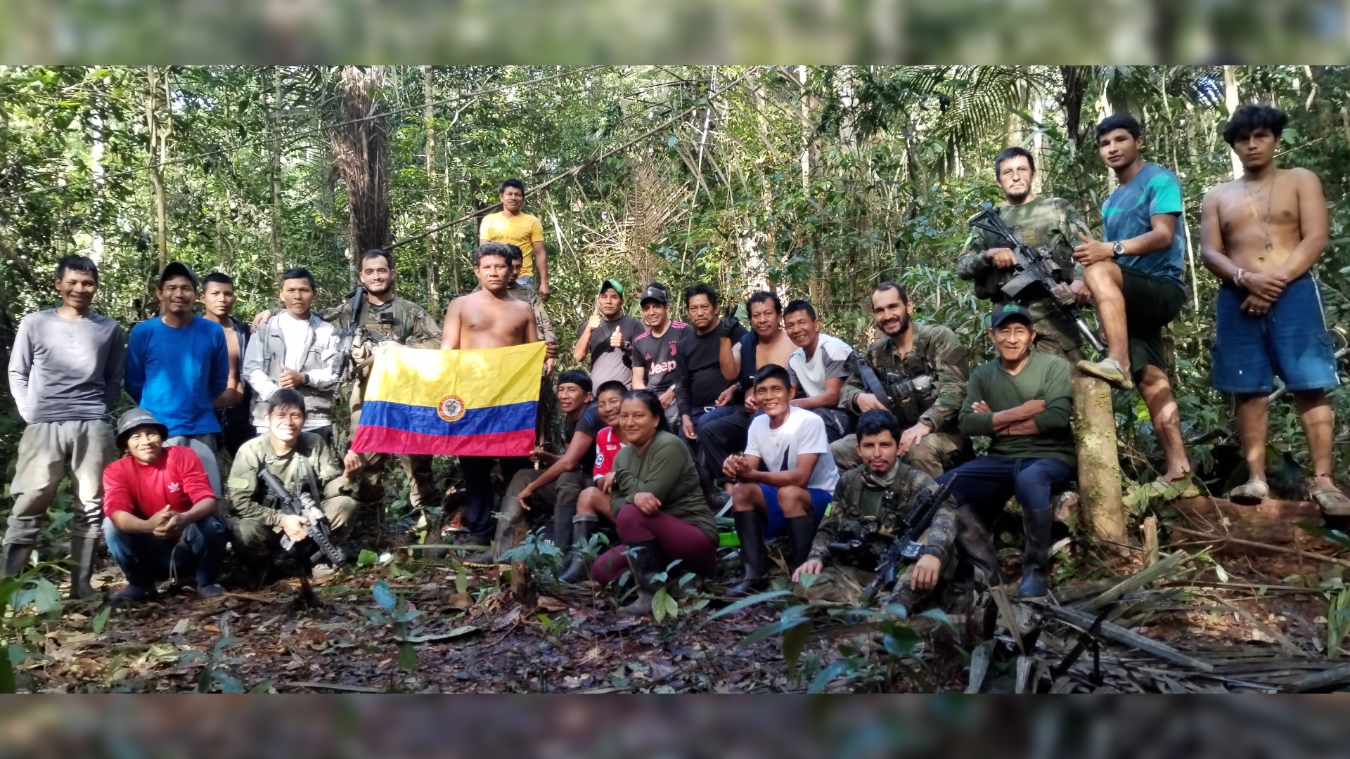 The Indigenous search team and Colombian military stand together in the jungle with the national flag. 