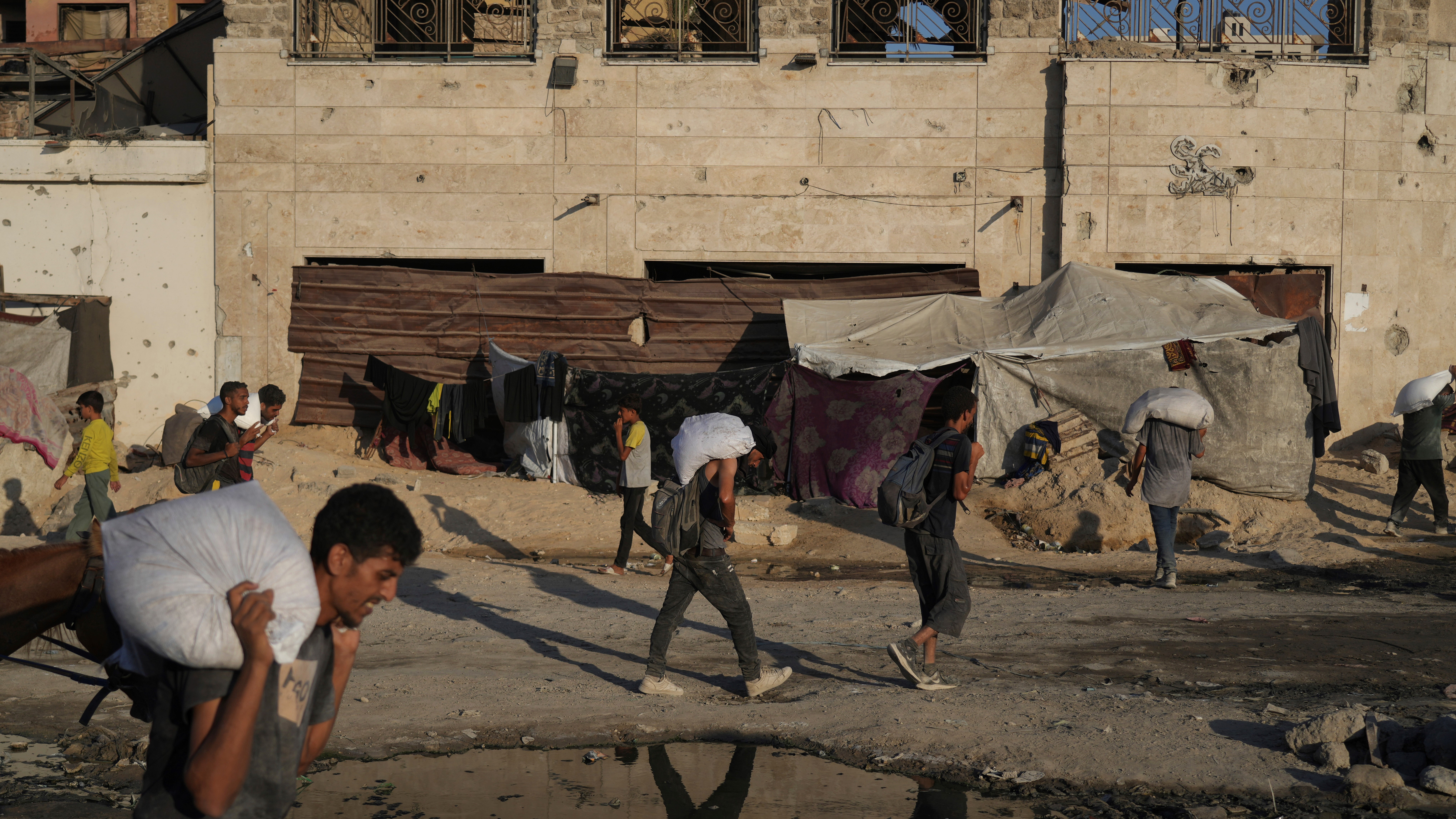 Palestinians carry sacks of flour unloaded from a humanitarian aid convoy that reached Gaza City from the northern Gaza Strip, Sunday, Aug. 24, 2025.
