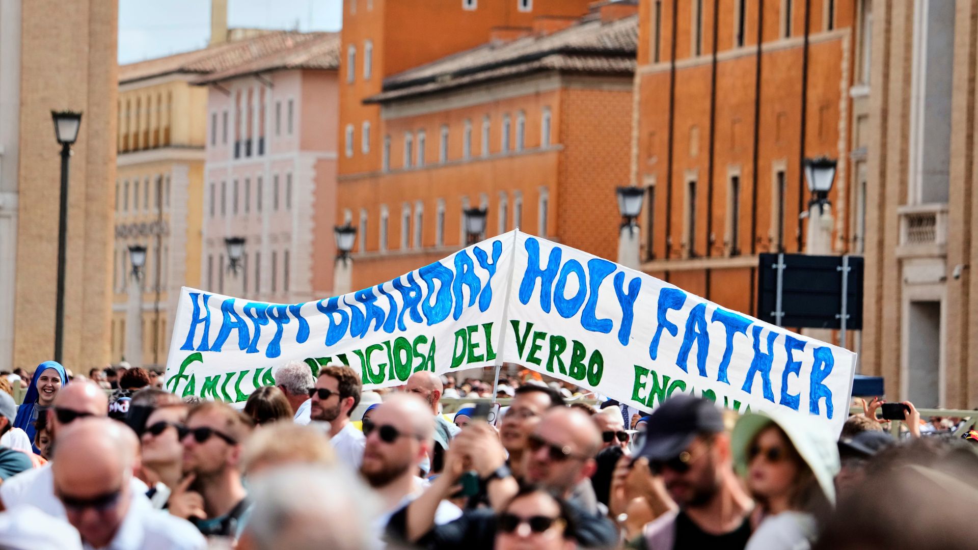 Faithful display a banner wishing happy 70th birthday to Pope Leo XIV as he appears to bless the faithful gathered in St. Peter's Square at the Vatican for the Angelus prayer.