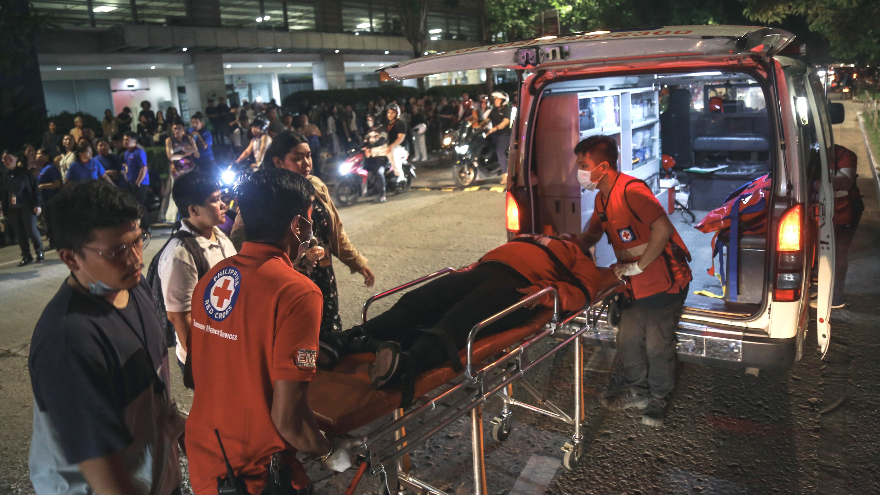 Medical workers load a resident into an ambulance as others stay outside buildings after a strong earthquake struck Cebu city, central Philippines, on Tuesday, Sept. 30, 2025.