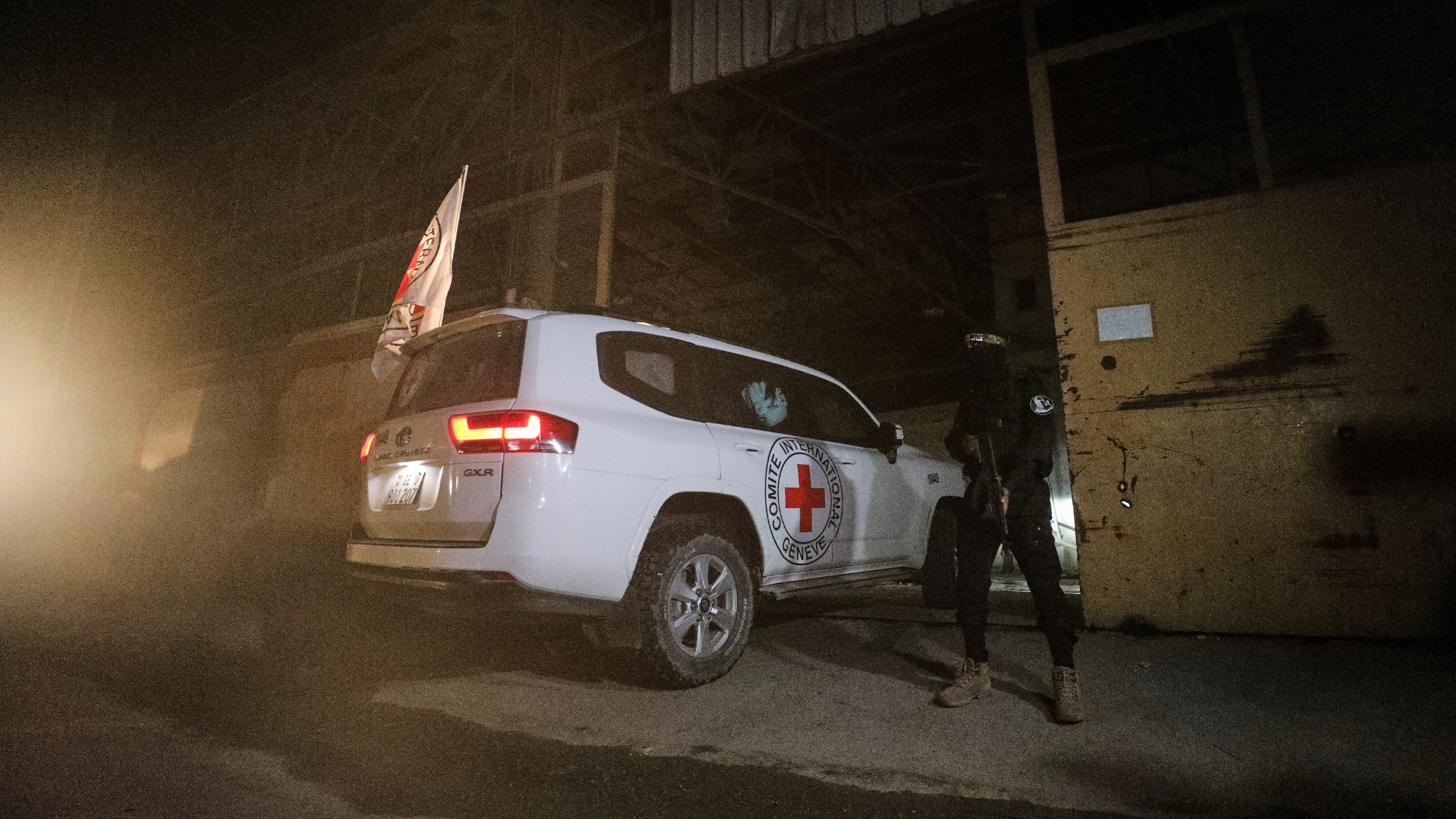 A gunman wearing the uniform of the al-Qassam Brigades stands guard as Red Cross vehicles allegedly transporting coffins containing the bodies of four deceased hostages leave a warehouse for Israel, in Gaza City, Tuesday, Oct. 14, 2025.