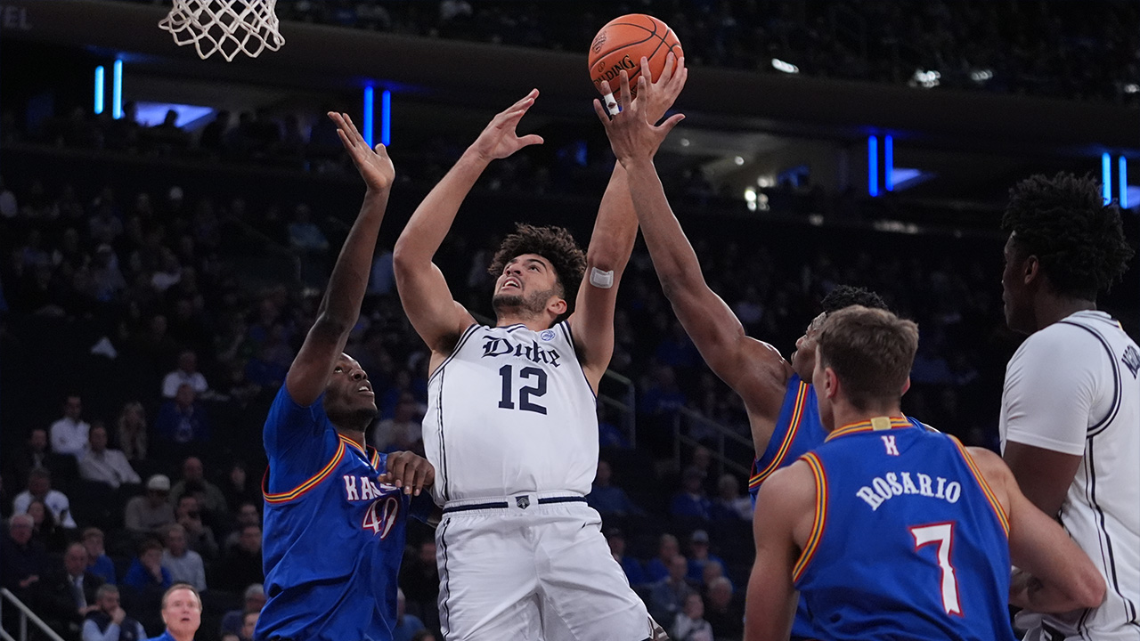 Duke's Cameron Boozer (12) drives past Kansas' Flory Bidunga (40) and Kohl Rosario (7) during NCAA college basketball game Tuesday, Nov. 18, 2025, in New York.