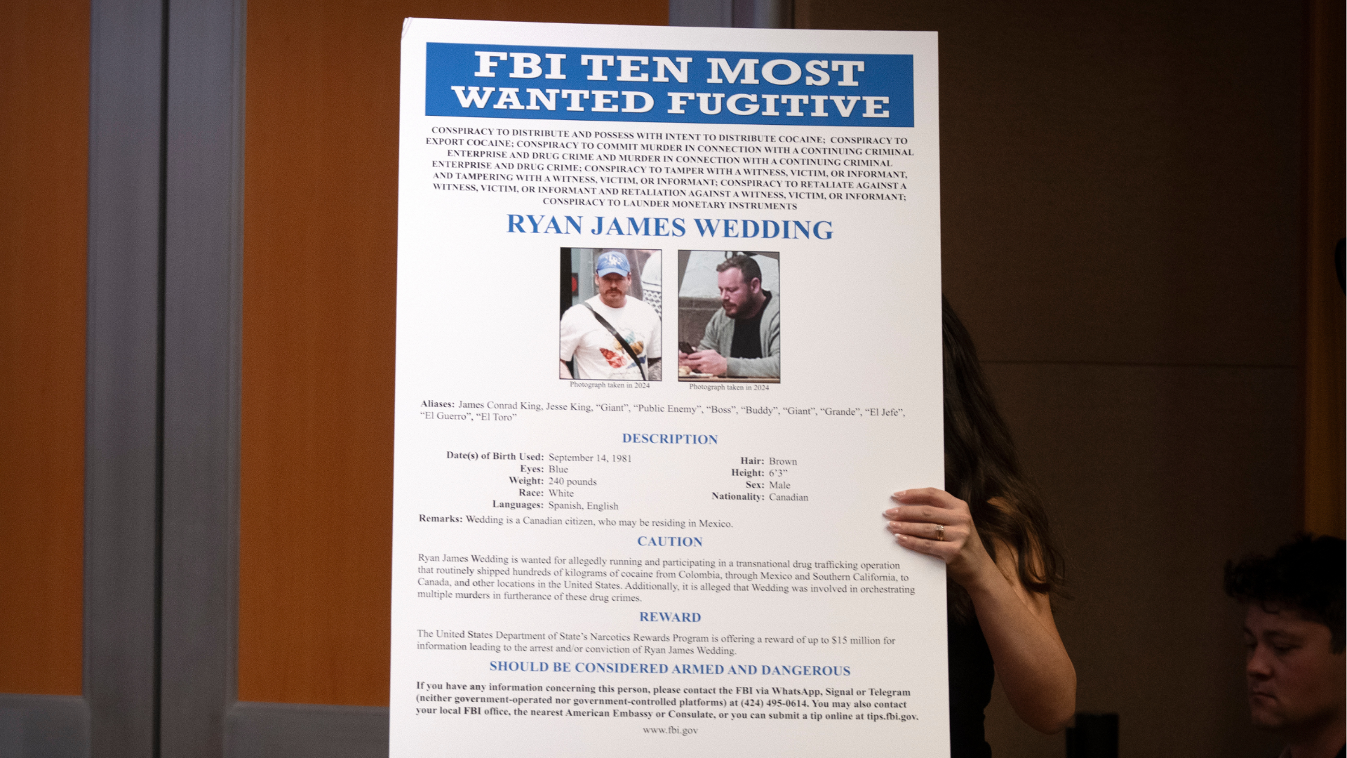 A staff member moves a wanted poster for Canadian fugitive Ryan James Wedding during a news conference at the Department of Justice, Wednesday, Nov. 19, 2025, in Washington.