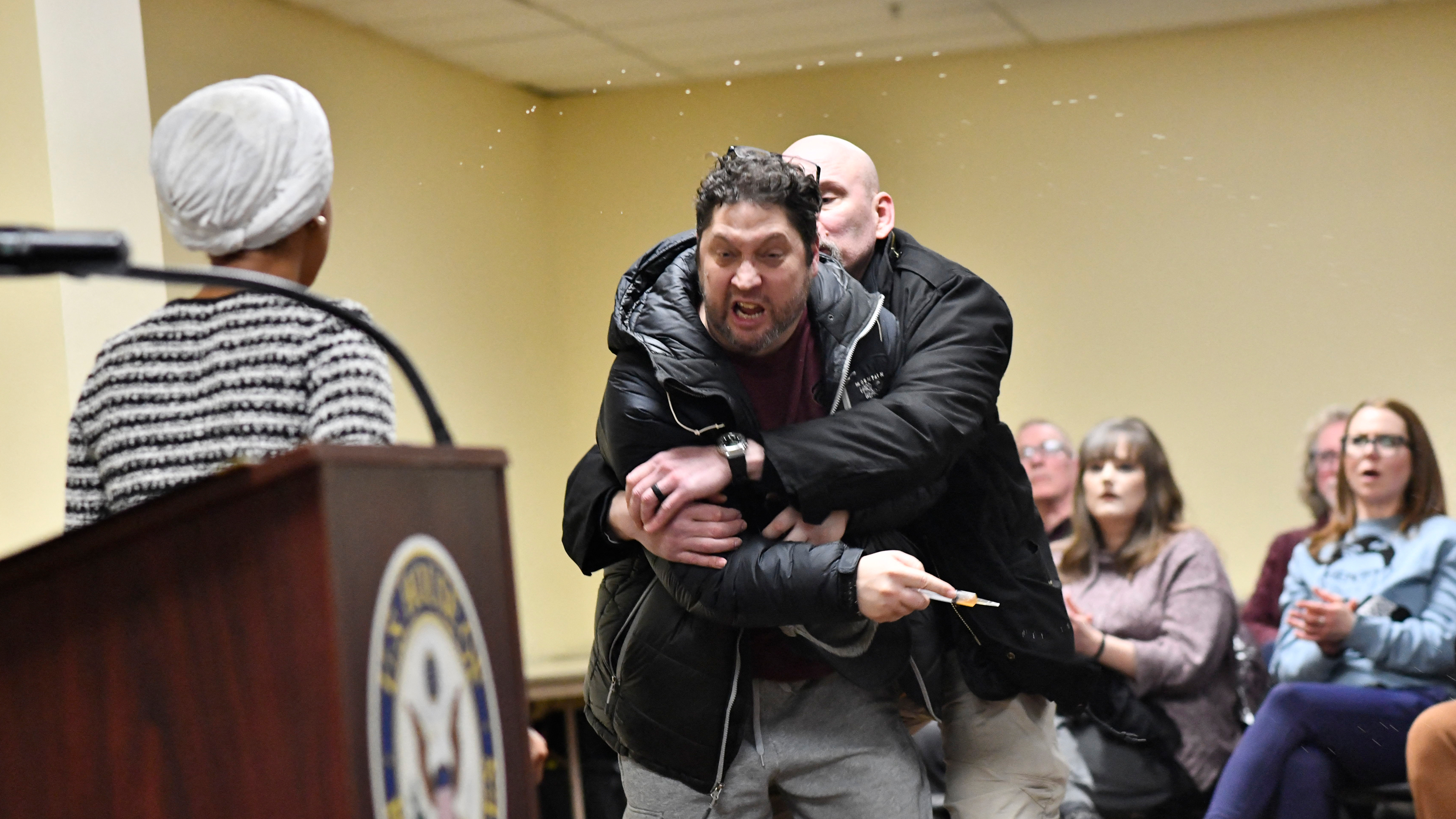 A man is tackled after spraying an unknown substance at US Representative Ilhan Omar (D-MN) (L) during a town hall she was hosting in Minneapolis, Minnesota, on January 27, 2026. 