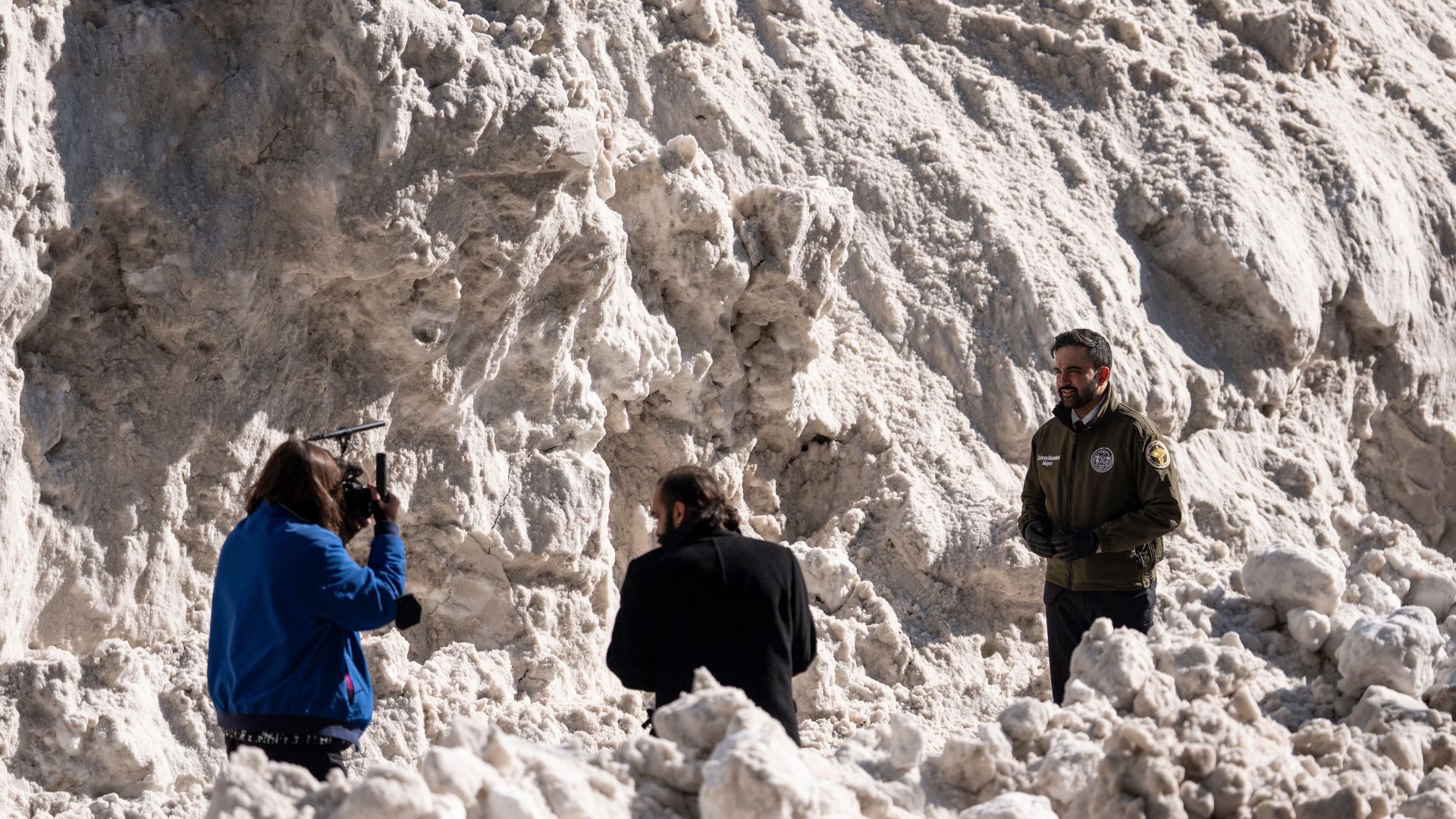 Mayor Zohran Mamdani stands backdropped by a pile of snow while recording a video during a visit to the Department of Sanitation's snow melting operations.
