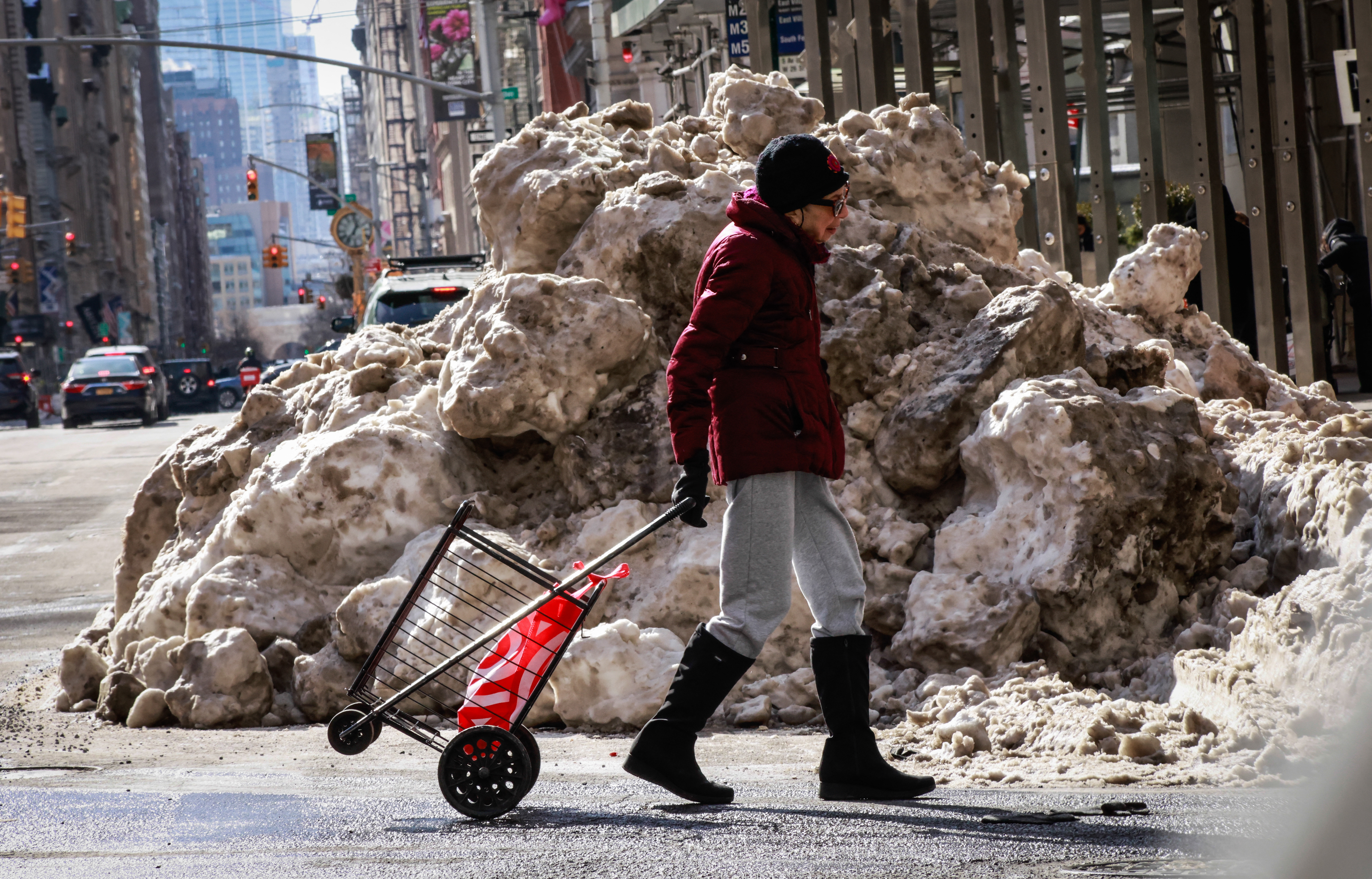 Snow piles cover the sidewalk as a person crosses the street in Midtown Manhattan in New York City on February 1, 2026.
