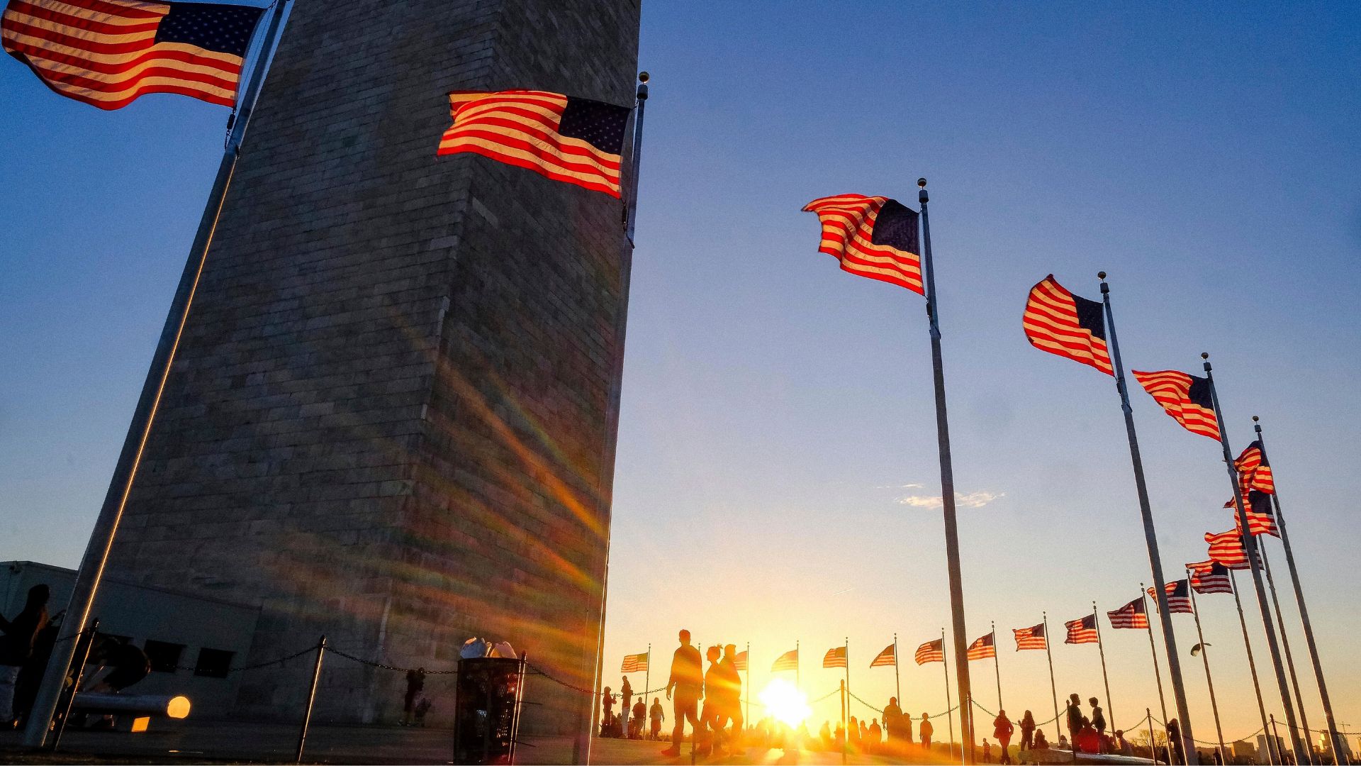 FILE - Tourists walk around the base of the Washington Monument on Presidents Day weekend as the sunsets, Feb. 19, 2017, in Washington.