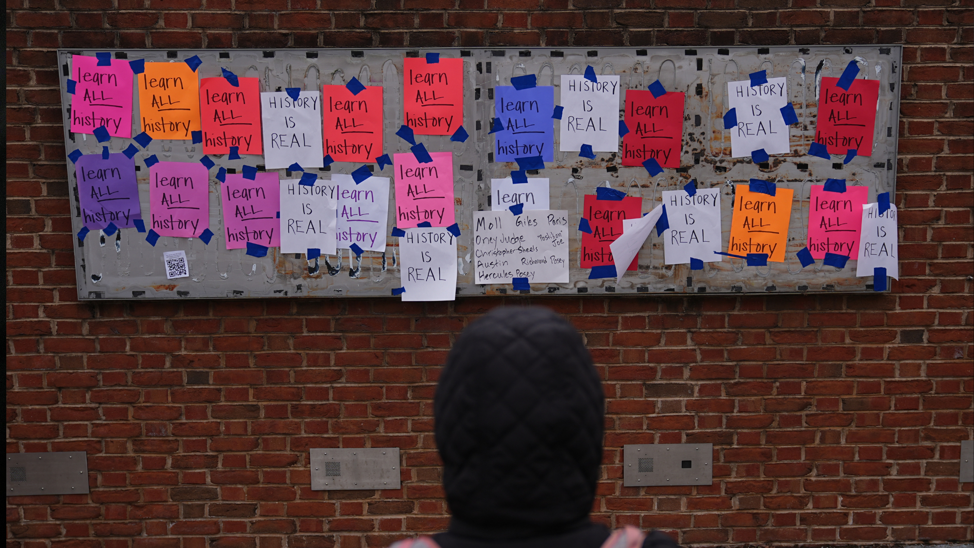 A person views posted signs on the locations of the now removed explanatory panels that were part of an exhibit on slavery at President's House Site in Philadelphia, Jan. 23, 2026.