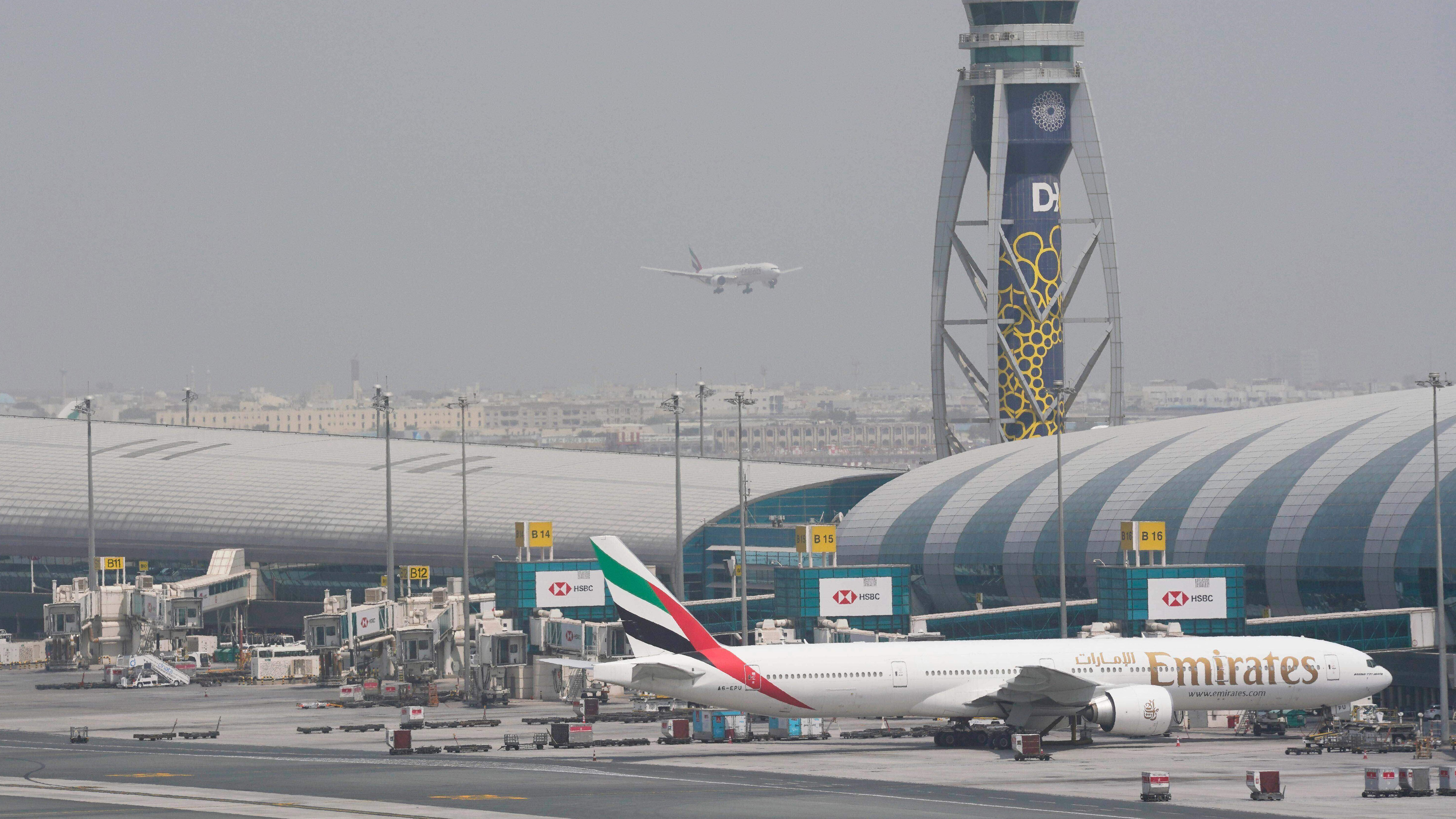 An Emirates Boeing 777 stands at the gate at Dubai International Airport as another prepares to land on the runway in Dubai, United Arab Emirates, Aug. 17, 2022.