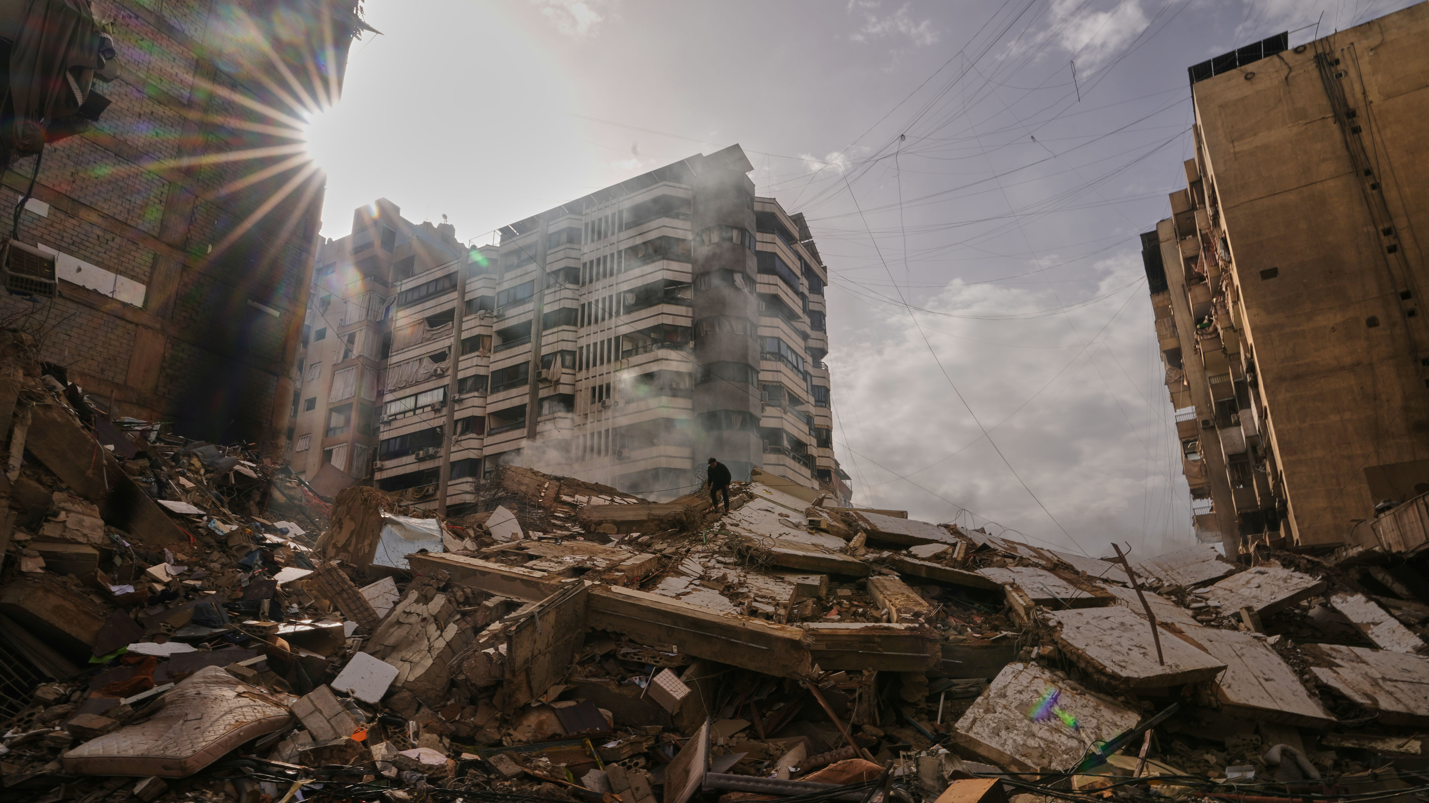 A man stands atop the rubble as smoke rises from a building destroyed in an Israeli airstrike in Dahiyeh, Beirut's southern suburbs, Lebanon, Saturday, March 14, 2026.
