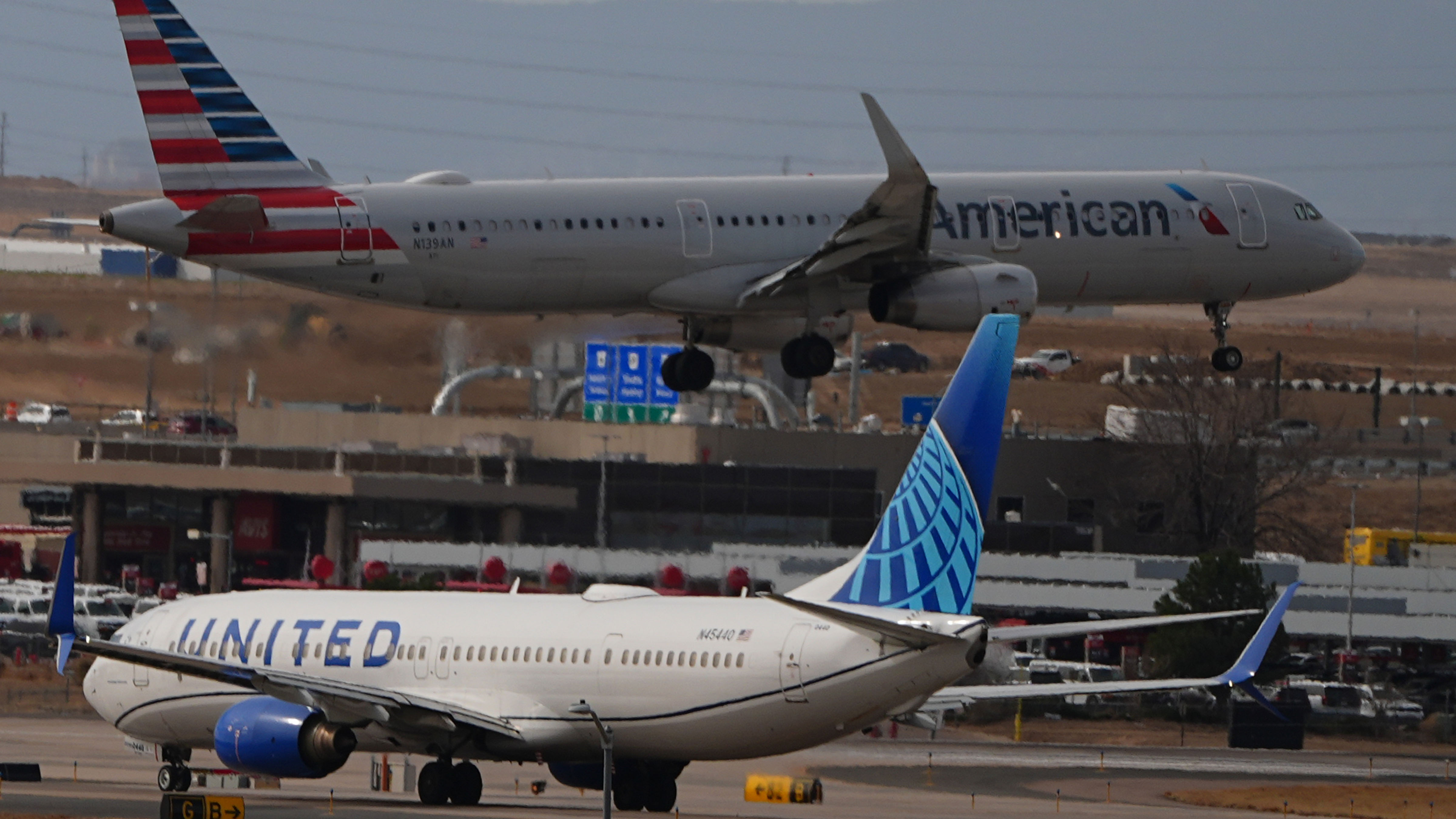 An American Airlines jetliner lands on a runway as a United Airlines plane waits for clearance to take off as high winds strafe Denver International Airport Thursday, March 12, 2026, in Denver.