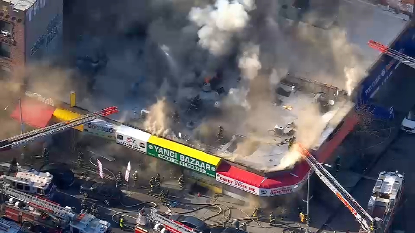 Firefighters battling flames on roof of building housing row of businesses in Midwood