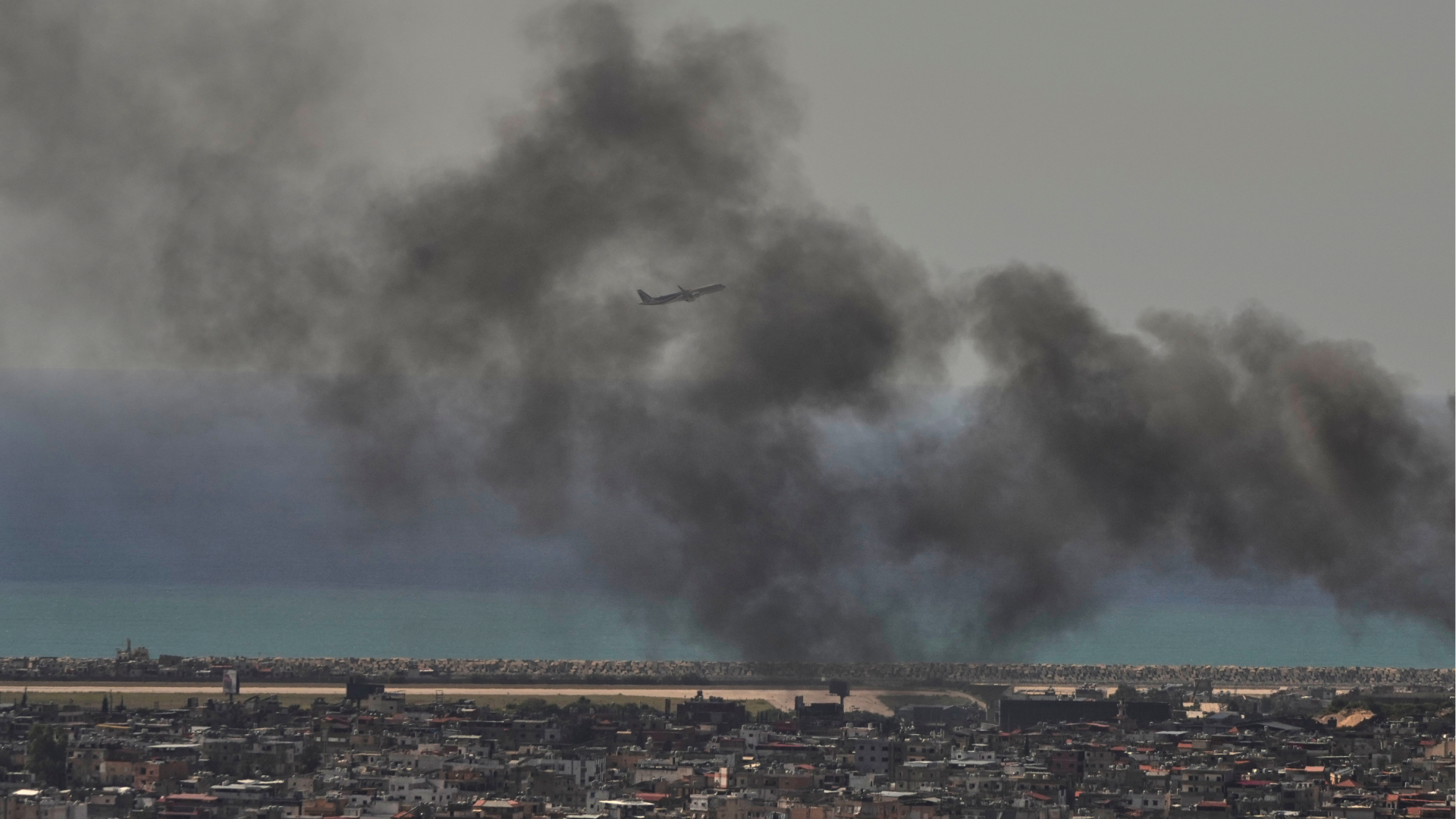 A Middle East Airlines plane takes off from Rafik Hariri International Airport as smoke rises from the site of an Israeli airstrike in Dahiyeh, Lebanon, Tuesday, March 17, 2026.