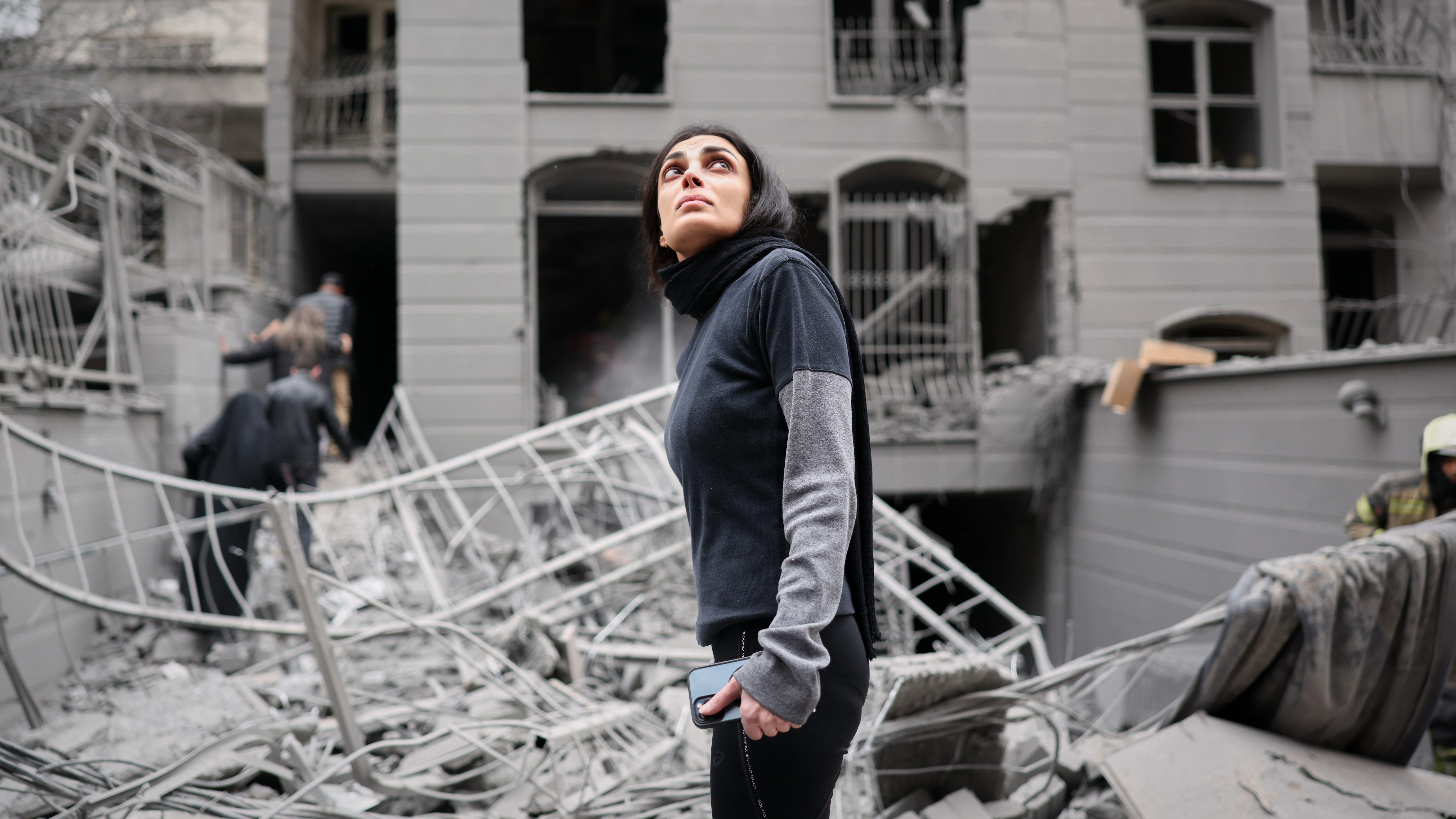 A woman looks up at the site of a strike that hit a residential building amid the U.S.-Israeli military campaign in Tehran, Iran, Saturday, March 28, 2026.