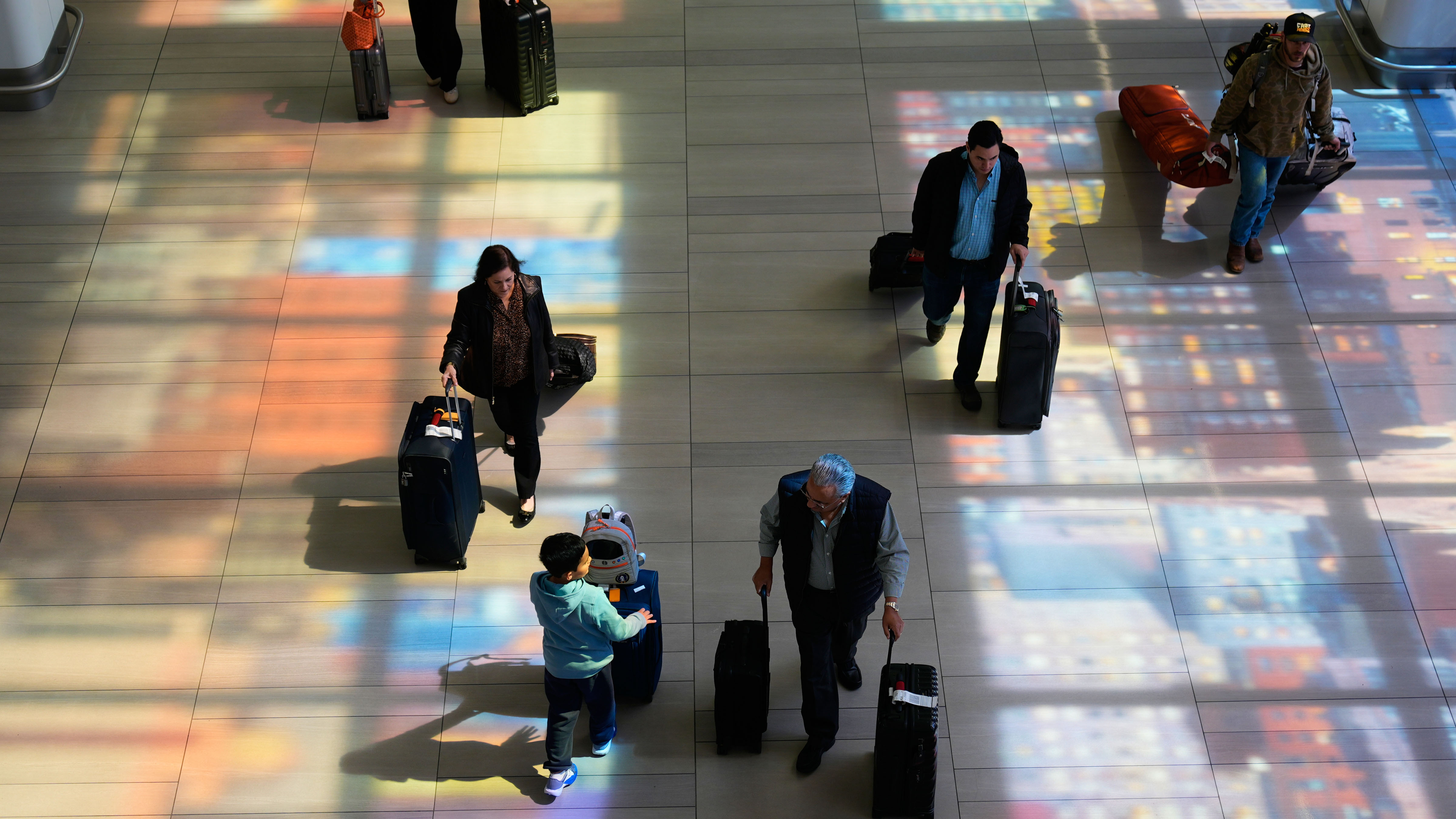 Stained-glass windows cast colorful shadows on the floor as travelers walk through LaGuardia Airport in New York, Monday, March 30, 2026.