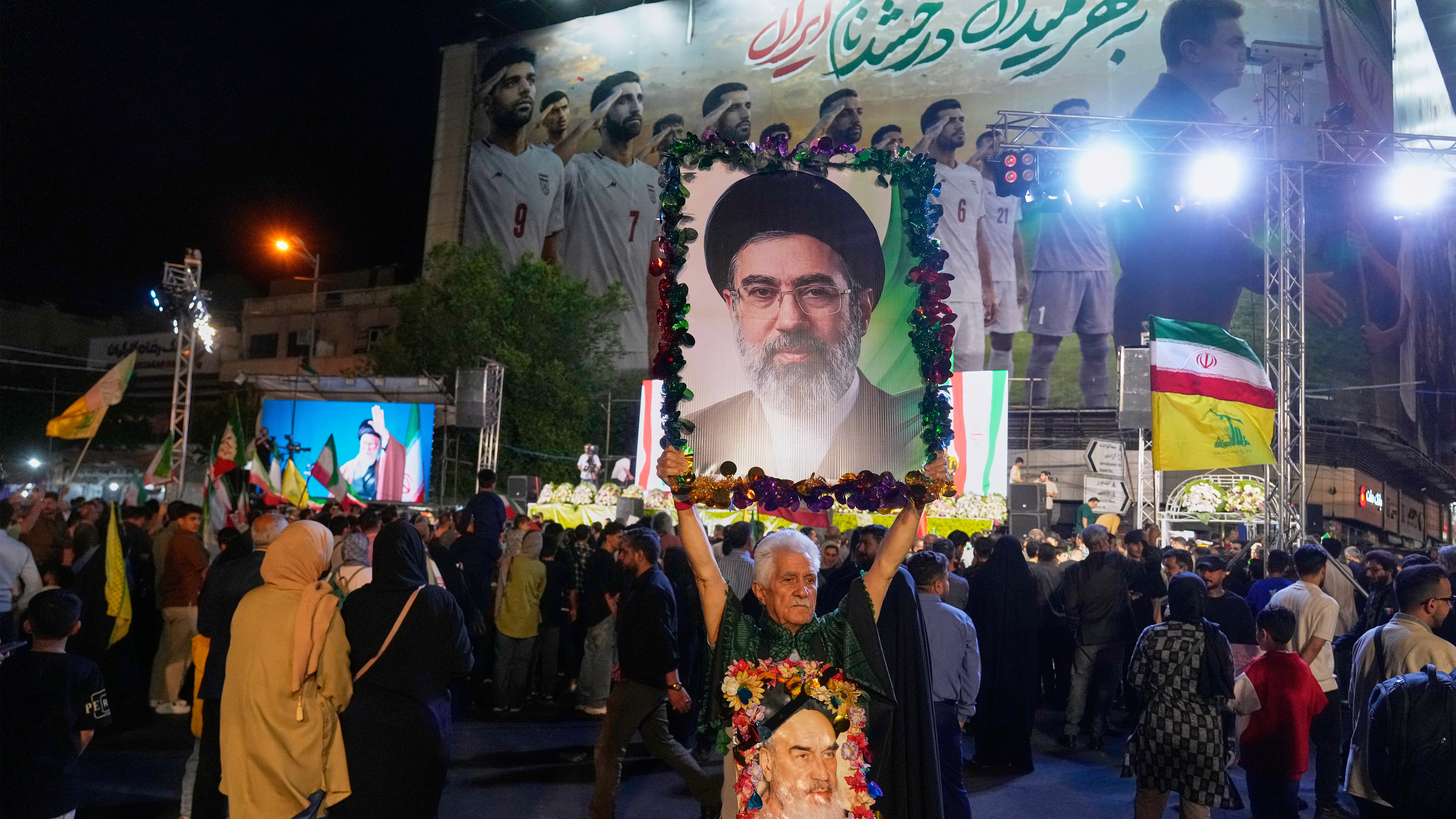 Backdropped by a billboard of Iran's national soccer team, a man holds a portrait of Supreme Leader Ayatollah Mojtaba Khamenei.