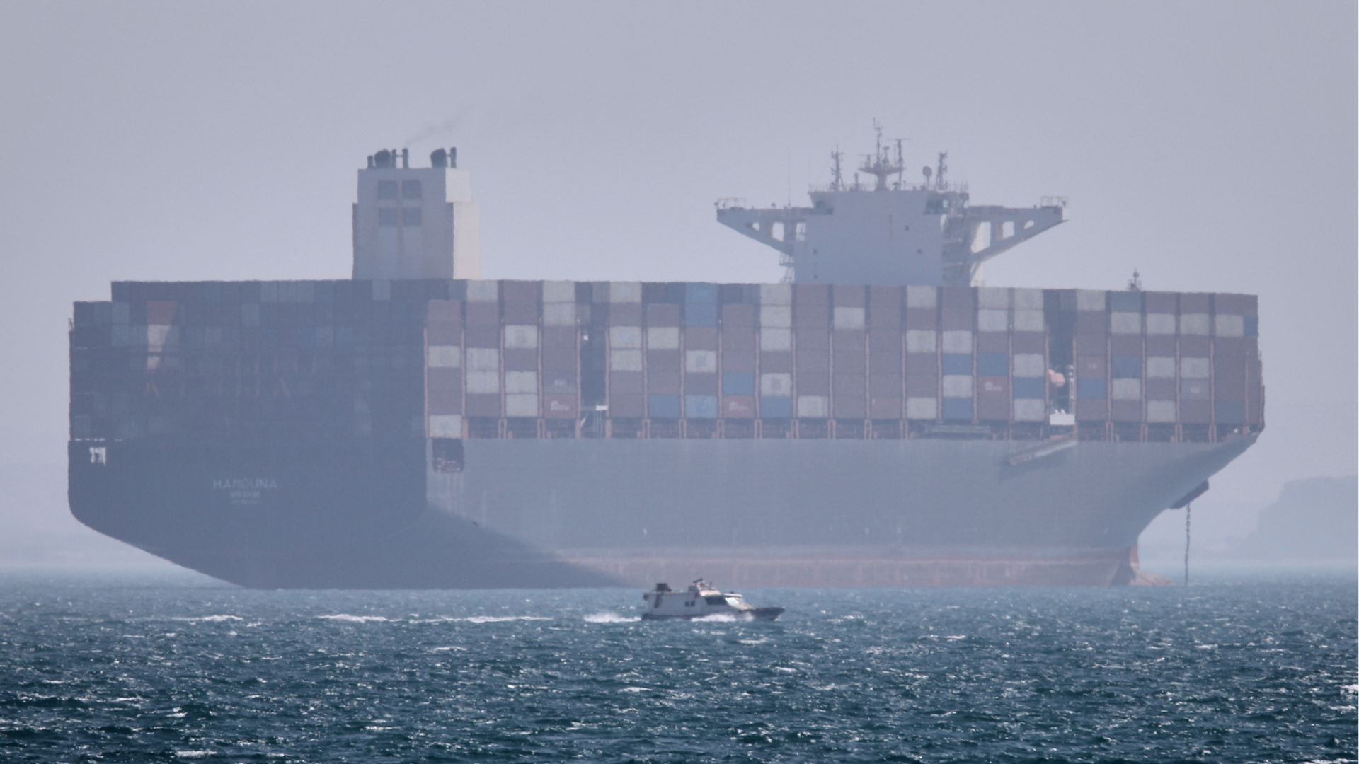 A container ship sits at anchor as a small motorboat passes in the foreground in the Strait of Hormuz off Bandar Abbas, Iran, Saturday, May 2, 2026.