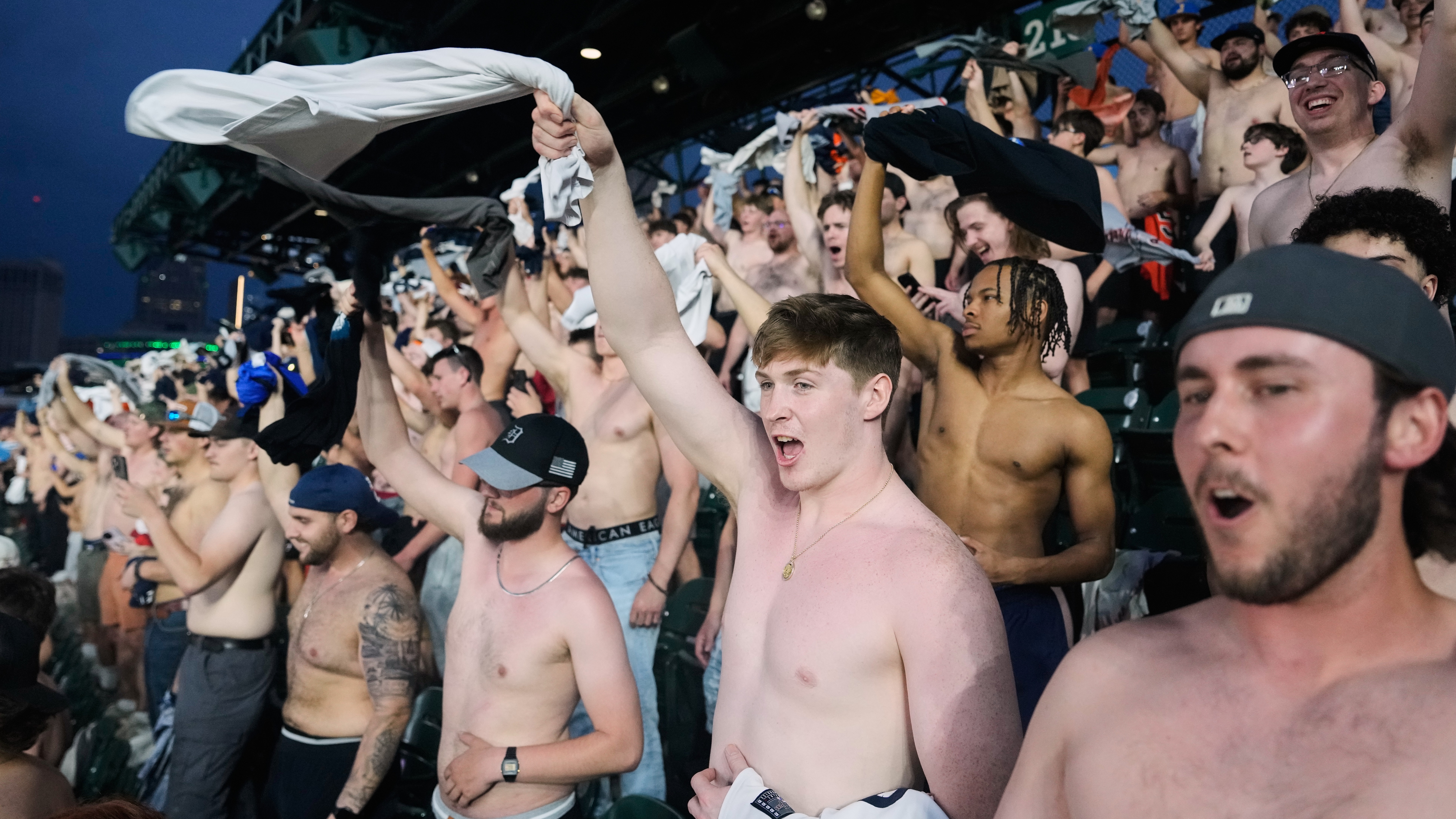 Fans cheer with their shirts off after heading to the upper deck outfield seating during the ninth inning of a baseball game between the Detroit Tigers and Cleveland Guardians