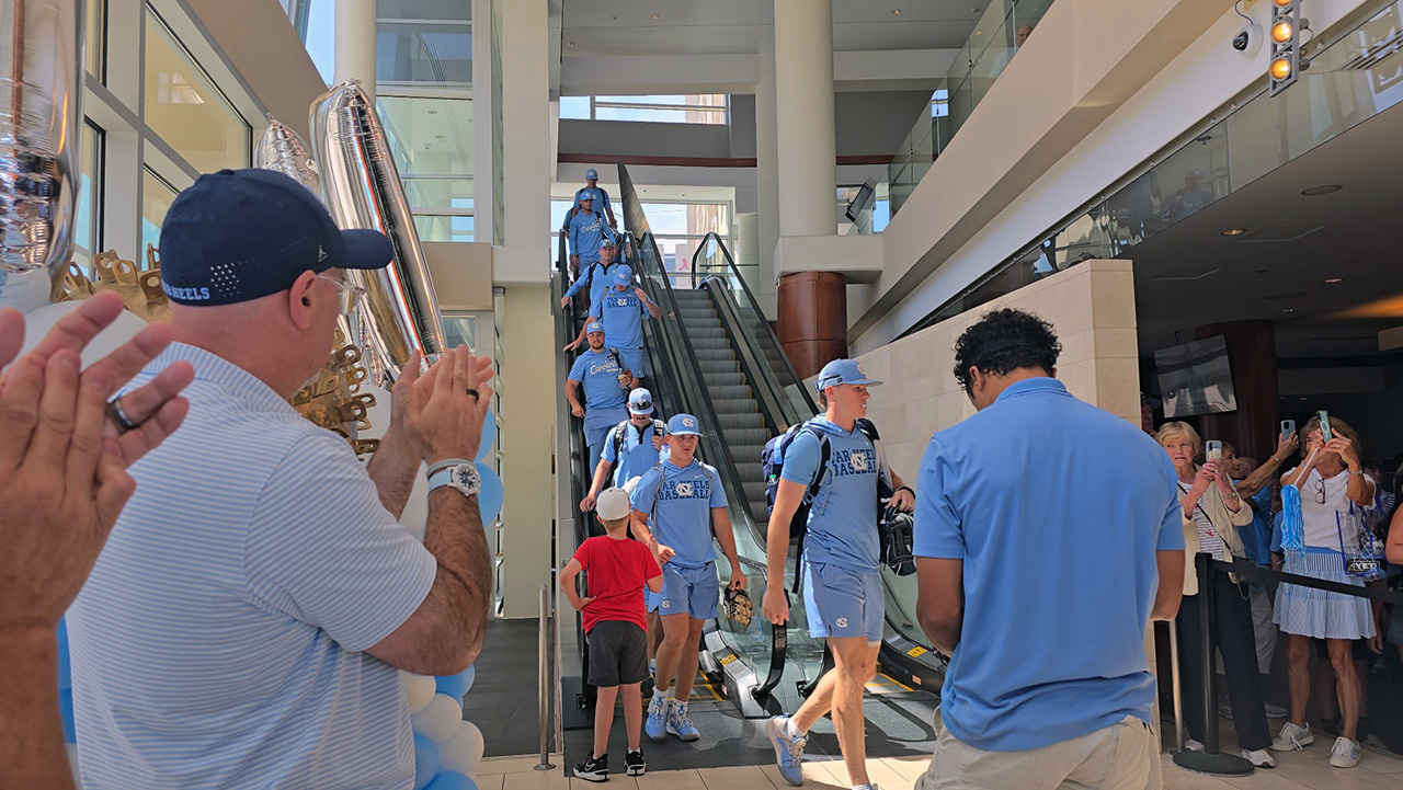 David Hill, in the red shirt, greets Tar Heels baseball players in Omaha, Nebraska.