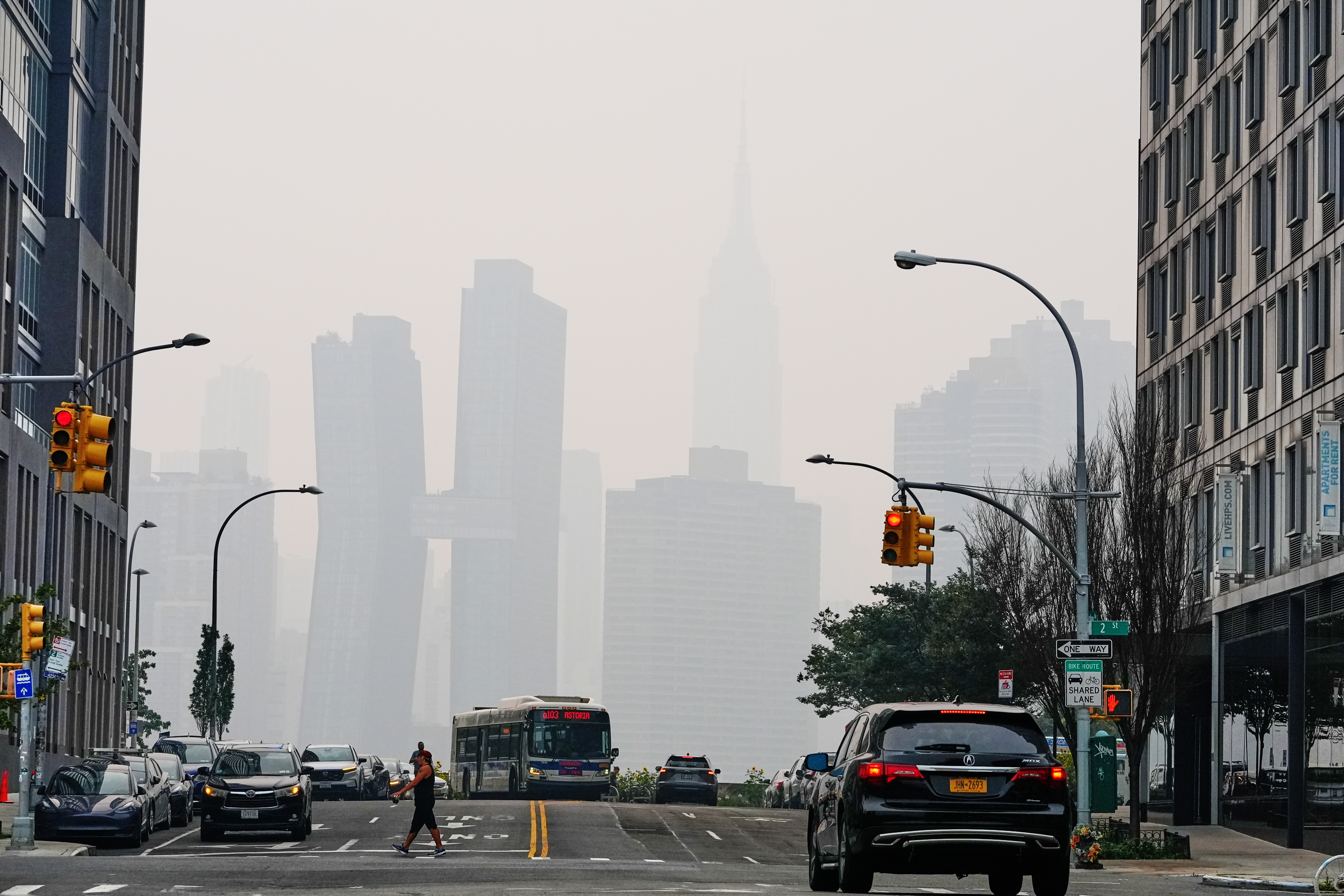 Pedestians cross Borden Avenue as the NYC skyline is obscured during poor air quality due to smoke from Canadian wildfires, July 16, 2026, in the Queens borough of New York.