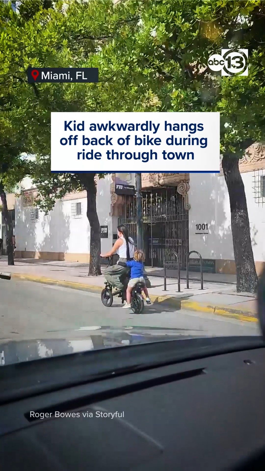 Kid awkwardly hangs off back of bike during ride through town