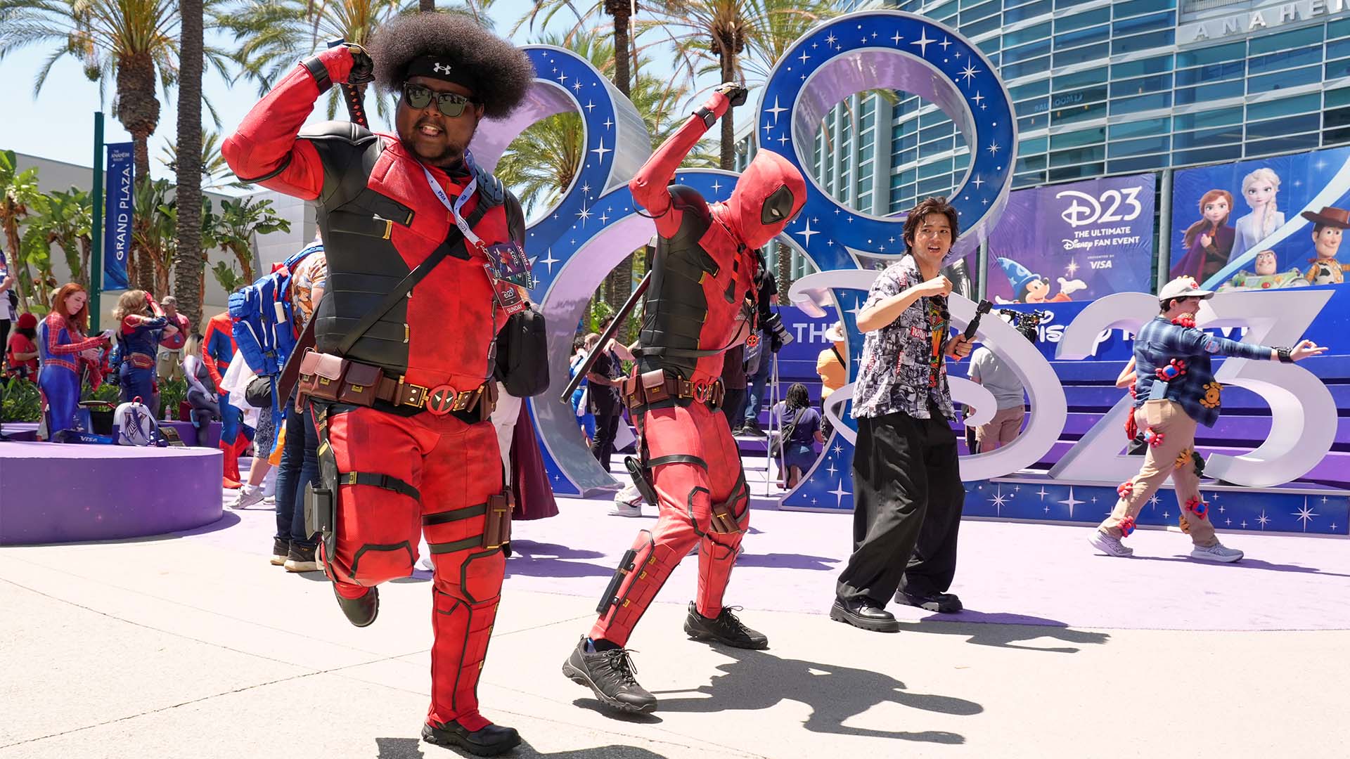 Mohamed Obsidye, left, of Columbus, Ohio, dressed as his own superhero character "Afro-Pool," leads a dance outside the entrance to D23 on Aug. 14, 2026 in Anaheim, Calif.