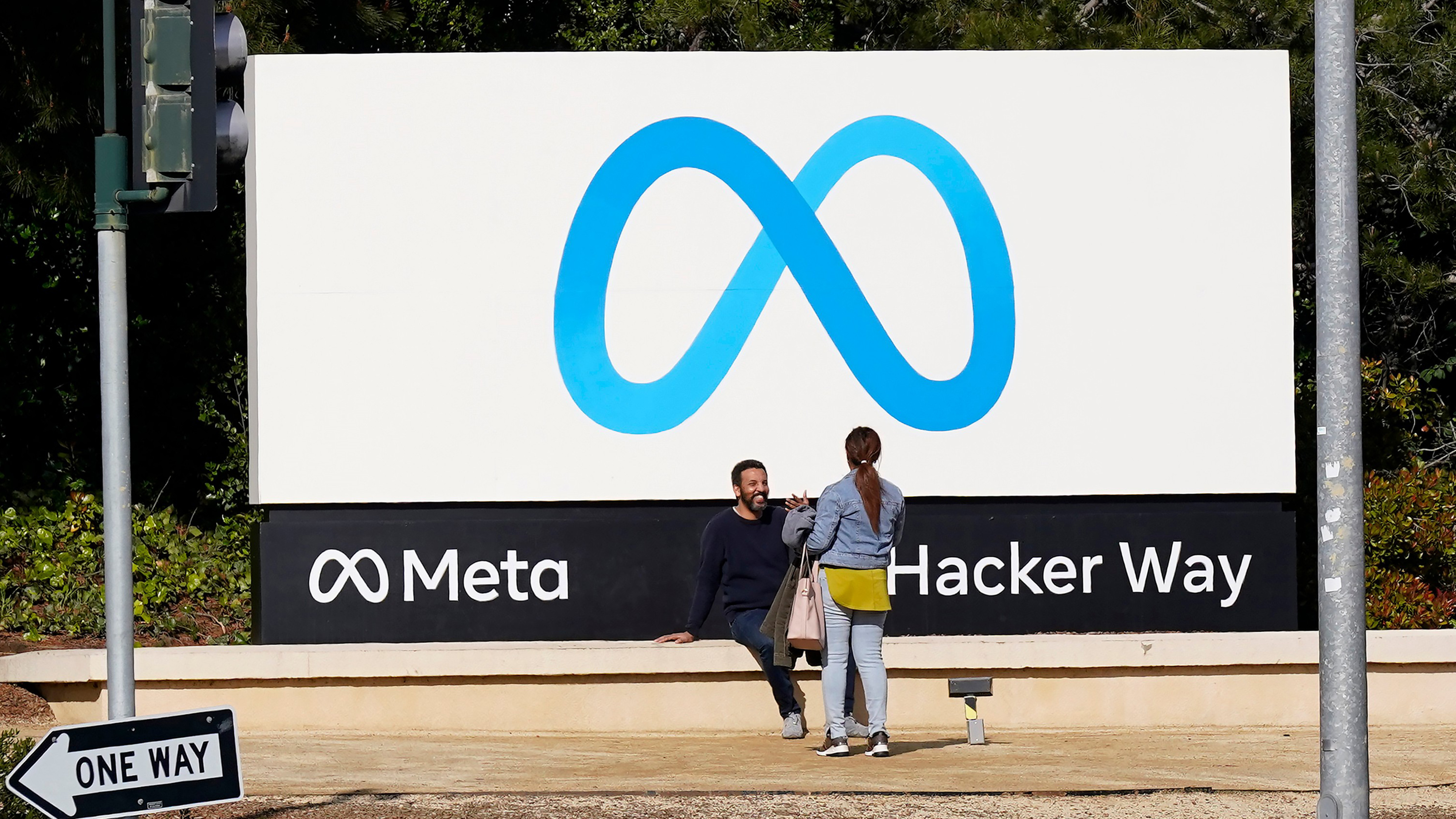 People talk near a Meta sign outside of the company's headquarters in Menlo Park, Calif., March 7, 2023. 