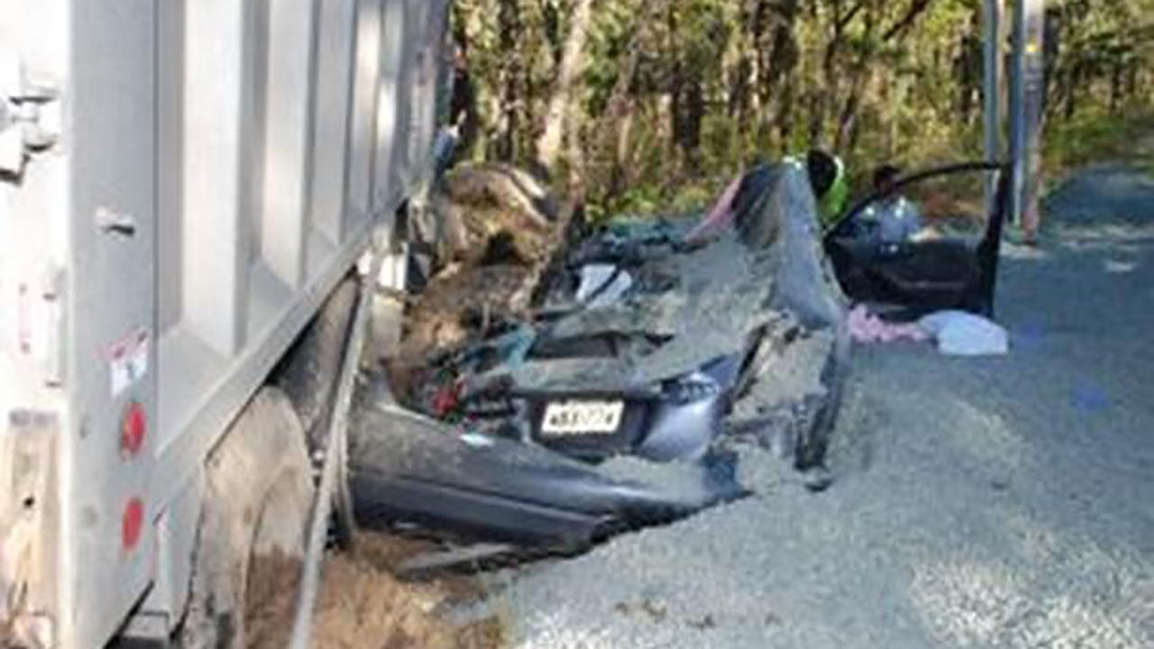 Driver rescued after truck overturns, spills stone on car
