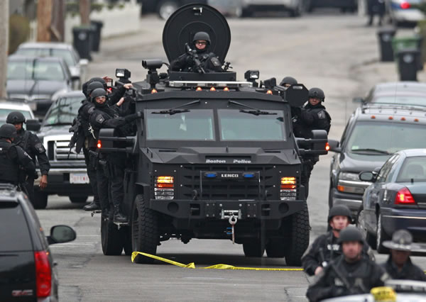 Police patrol through a neighborhood in Watertown, Mass., while searching for a suspect in the Boston Marathon bombings, Friday, April 19, 2013. The bombs that blew up seconds apart near the finish line of the Boston Marathon left the streets spattered with blood and glass, and gaping questions of who chose to attack and why.