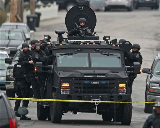Police in tactical gear arrive on an armored police vehicle as they surround an apartment building while looking for a suspect in the Boston Marathon bombings in Watertown, Mass., Friday, April 19, 2013.