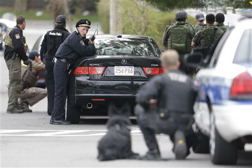 Police officers take cover as they conduct a search for a suspect in the Boston Marathon bombings, Friday, April 19, 2013, in Watertown, Mass.