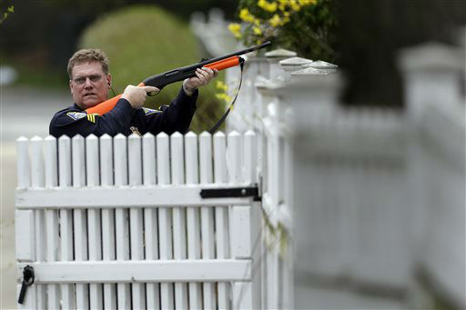 A police officer points his weapon at a residence as he conducts a search for a suspect in the Boston Marathon bombings, Friday, April 19, 2013, in Watertown, Mass.