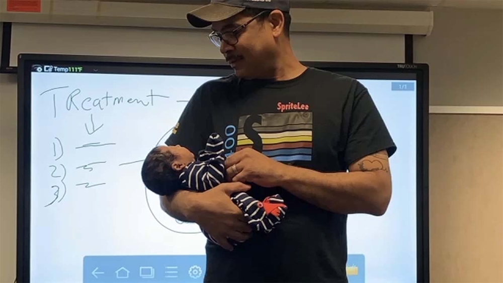 Professor holds baby during lecture so mom can take notes